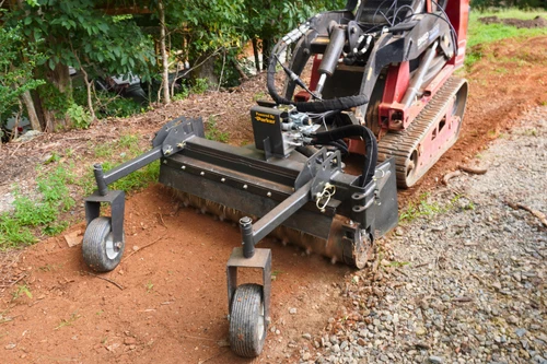CID Multi-Purpose Power Rake for Mini Skid Steers | Small excavator with a attachments on a dirt path