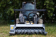 Baumalight MS560 with spiral tooth pattern - Backhoe loader with attachment on grassy area with trees in the background