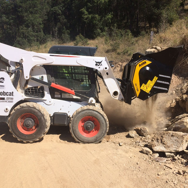 Bobcat MB-L160 skid steer loader with a clamshell attachment breaking up rocks on a dirt surface.