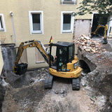 Caterpillar-305 excavator in front of a building under construction with visible demolition work.