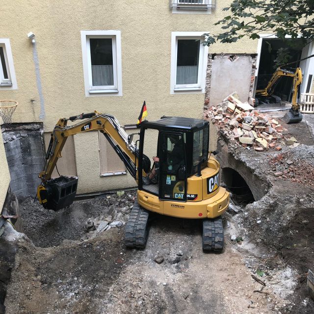 Caterpillar-305 excavator in front of a building under construction with visible demolition work.