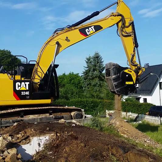 Caterpillar BF80.3 excavator at a construction site with trees and a house in the background.