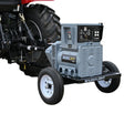 A Baumalight KR65 - 65 kW Tractor PTO Generator, with a tractor and a PTO shaft attached to it. The generator is mounted on the tractor with a label and wheels for mobility.