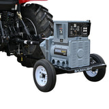 A Baumalight KR65 - 65 kW Tractor PTO Generator, with a tractor and a PTO shaft attached to it. The generator is mounted on the tractor with a label and wheels for mobility.