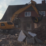 Liebherr MB-L200 excavator in front of a brick house with rubble