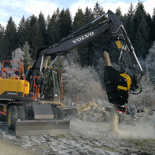 Volvo EW160E operating in a forested area with trees and ground visible.