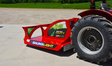A red Baumalight CP572 rotary brush cutter for tractor with black tires and a push bar, located outdoors on a pavement.