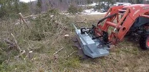 Backhoe loader in a field with trees and snow