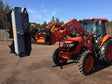 Red tractor with attachments on a paved surface with trees in the background