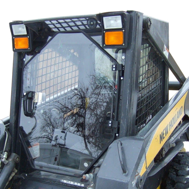 A New Holland skid steer door made of heavy-duty polycarbonate, featuring a black color with a clear front, mounted on a skid steer loader with visible orange lights and branding.
