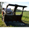Loflin Fabrication | Mini Skid Steer Grapple Bucket | A black Loflin Fabrication Mini Skid Steer Grapple Bucket placed on grass with a clear sky and trees in the background.